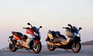 Dwa skutery BMW C650 Sport w kolorach czerwonym i brązowym stoją na tle zachodzącego słońca.