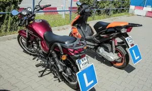 Dwa pojazdy z literą "L" na tablicy, gotowe do nauki jazdy. Czerwony motorower i pomarańczowy skuter.