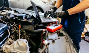 Mechanik diagnozuje problem z silnikiem 4t, który się dusi po dodaniu gazu. Na laptopie analizuje dane, obok leży multimetr.