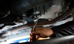 Dłoń mechanika dokręca kluczem nasadowym korek spustowy oleju. Ważne jest, z jaką siłą dokręcać korek spustowy oleju, by nie uszkodzić miski olejowej.