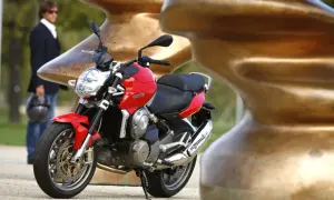 Czerwona Aprilia Mana 850 z chromowanym wydechem, obok mężczyzny w garniturze.