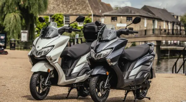 Dwa skutery Suzuki Burgman 125, jeden biały, drugi grafitowy, stoją obok siebie. Sprawdź suzuki burgman 125 cena!
