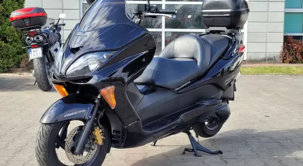 Czarny skuter Honda Forza 250 z kufrem na bagaż, zaparkowany przed budynkiem.