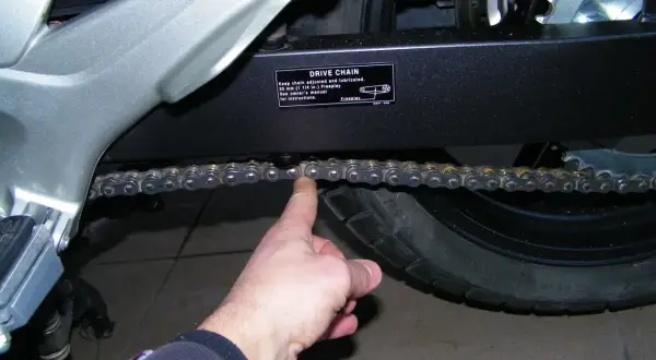 Sprawdzanie naciągu łańcucha w motocyklu. Palec pokazuje luźny łańcuch napędowy.