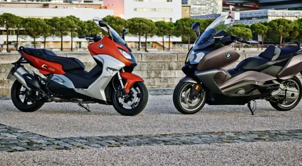 Dwa skutery BMW C650GT: jeden pomarańczowo-srebrny, drugi brązowy, stojące na kamiennym placu.