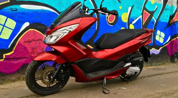 Czerwony skuter Honda PCX 125 na tle kolorowego graffiti. Mimo że jest to niezawodny model, warto pamiętać o jego awaryjności w ekstremalnych warunkach.