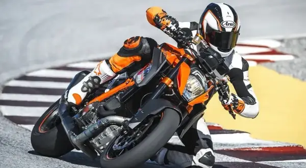 Motocyklista w kombinezonie pochyla się na torze wyścigowym na pomarańczowym motocyklu KTM Super Duke.