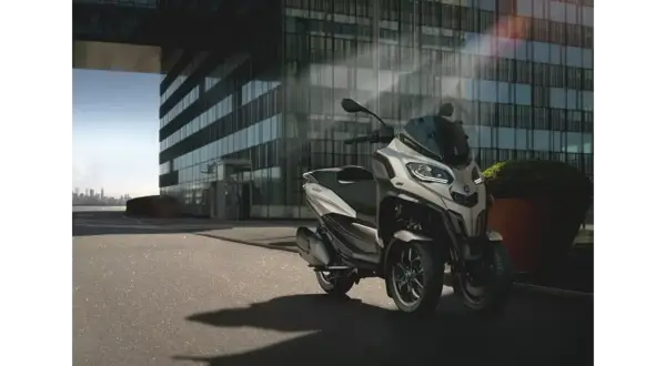 Nowoczesny Piaggio MP3, czy wersja 400 czy 500, parkuje przed szklanym budynkiem.
