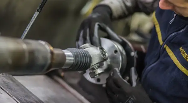 Mechanik w rękawiczkach montuje przegub wału kardana.