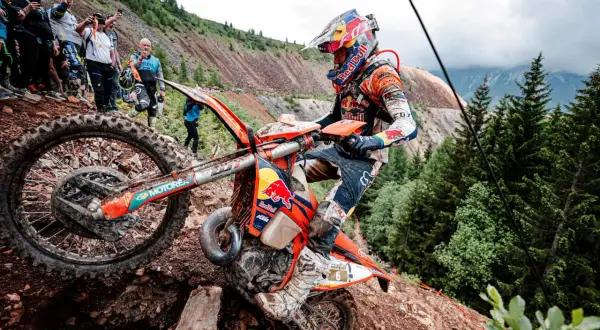 Motocyklista walczy z kamienistym podjazdem podczas Erzberg Rodeo. Widzowie obserwują zmagania na stromym zboczu.