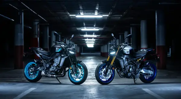 Dwa motocykle Yamaha MT, w tym jeden z niebieskimi felgami, prezentują swoją hyper naked estetykę w mrocznym garażu.