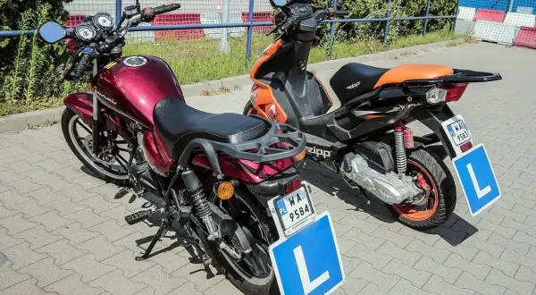 Dwa pojazdy z literą "L" na tablicy, gotowe do nauki jazdy. Czerwony motorower i pomarańczowy skuter.