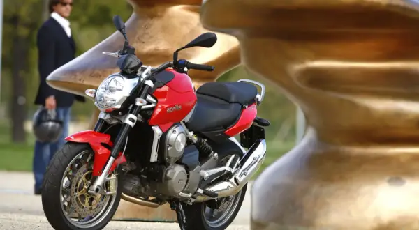 Czerwona Aprilia Mana 850 z chromowanym wydechem, obok mężczyzny w garniturze.
