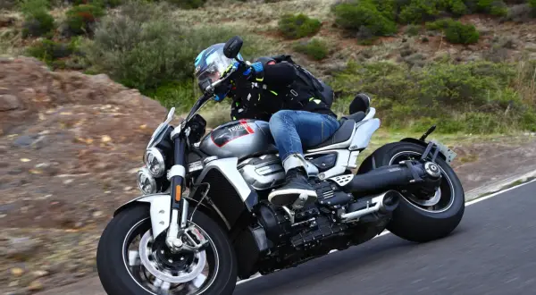 Motocyklista w kasku i kurtce jedzie na motocyklu Triumph Rocket 2 po krętej drodze wśród zieleni.