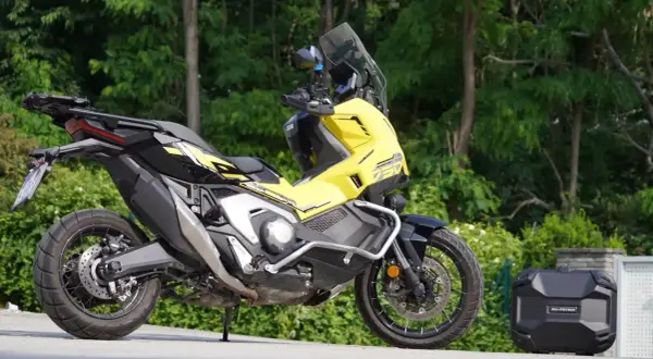 Żółty Honda X-ADV 750 z czarnymi akcentami, gotowy na przygodę. Obok bagażnik kufer.