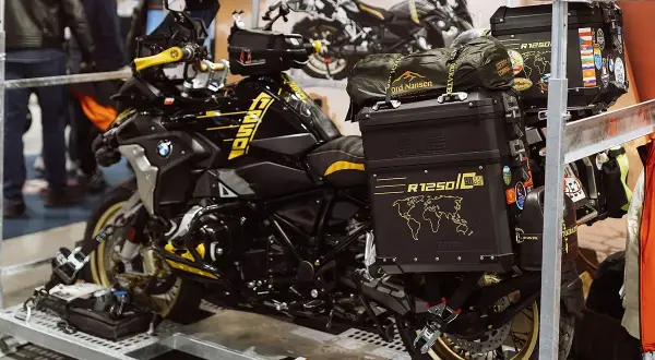 Czarny motocykl BMW R1250 GS z żółtymi akcentami, przygotowany do transportu motocykla w busie. Na kufrach mapy świata i naklejki.