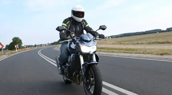 Motocyklista na Kawasaki Z750 2010 przemierza krętą drogę pośród pól.