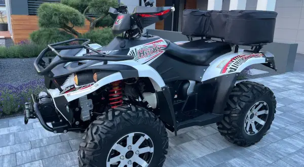 Hyosung TE 450 gotowy na przygodę. Biało-czarny quad z czerwonymi akcentami i bagażnikiem z tyłu.
