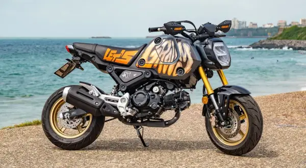 Niestandardowe malowanie baku motocykla z motywem płomieni i napisem "LET'S GO" na tle morza.