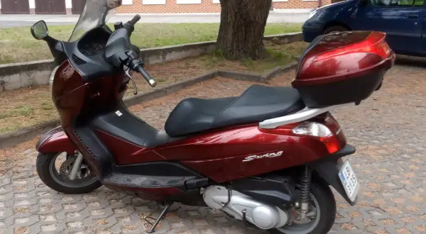 Ciemnoczerwony skuter Honda Swing 125 z czarnym siedzeniem i kufrem, zaparkowany na kostce brukowej.