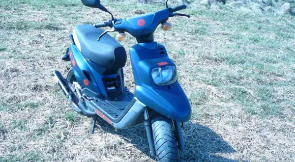 Niebieski skuter Yamaha MBK z czerwonymi akcentami stoi na trawiastym podwórku.
