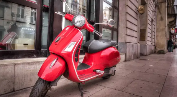 Czerwony skuter Vespa na chodniku. Karta motorowerowa od ilu lat? Warto sprawdzić, by legalnie poruszać się tym stylowym pojazdem.