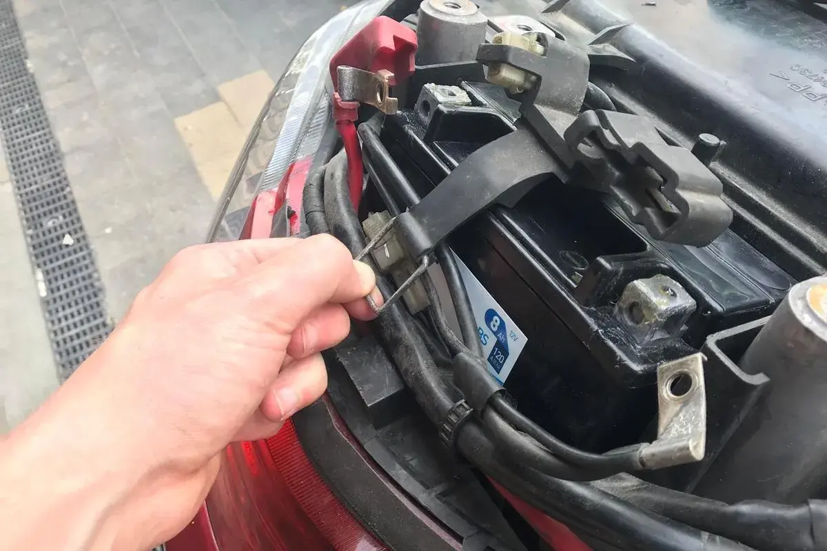 Dłoń przytrzymuje mocowanie akumulatora w skuterze. Widać jego umiejscowienie pod siedzeniem.