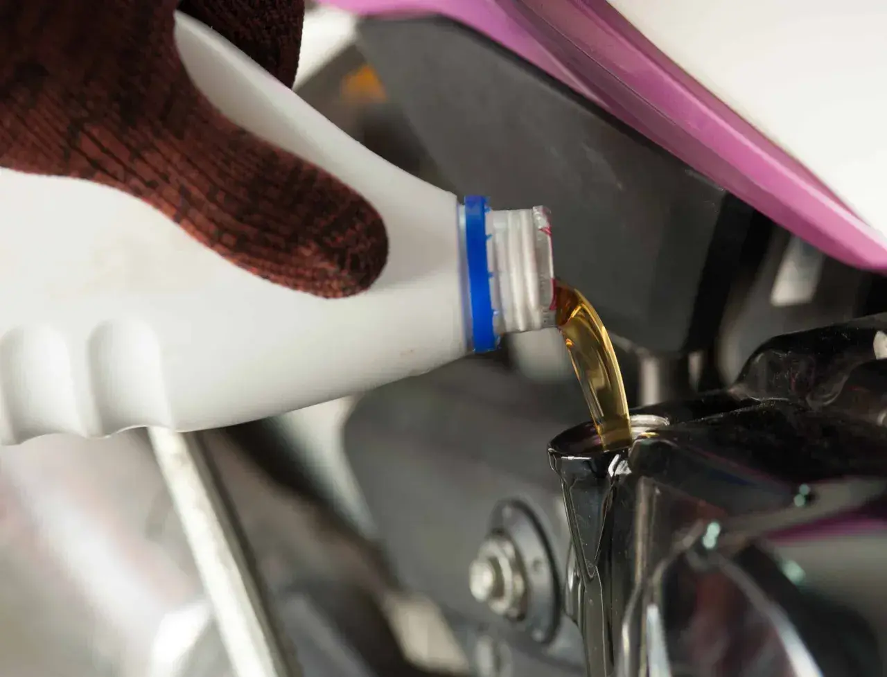 Rękawica wylewa olej do silnika motocykla. Pamiętaj, co ile wymieniać olej w motocyklu, by służył Ci długo.