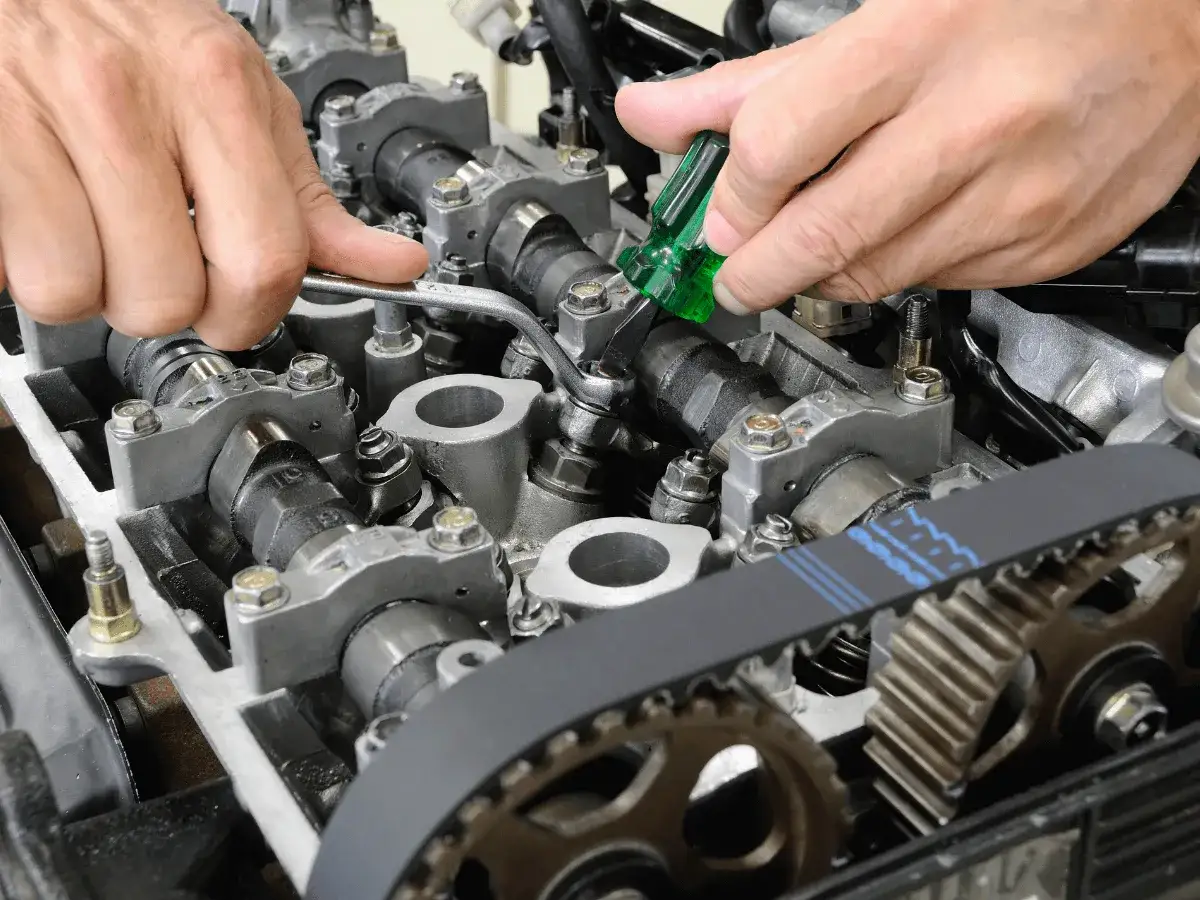 Mechanik dokonuje precyzyjnej regulacji zaworów silnika, używając klucza i śrubokręta.