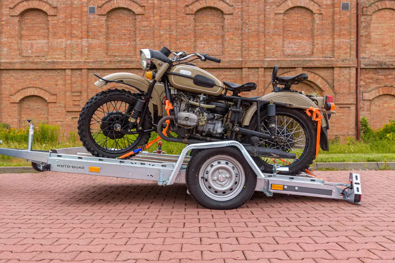 Motocykl Ural na przyczepie MOTO-QUAD, gotowy do dpd transportu. Ceglana ściana w tle.