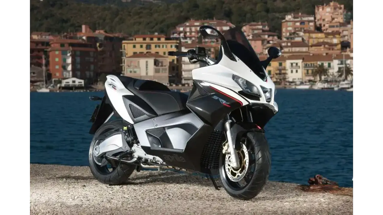 Sportowy skuter Aprilia SRV 850 na tle malowniczego włoskiego miasteczka nad wodą.