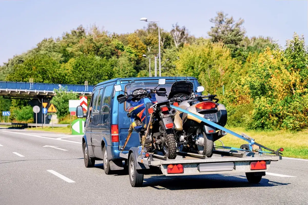 Transport motocykla w busie. Dwa motocykle na przyczepce za niebieskim busem, gotowe do podróży.