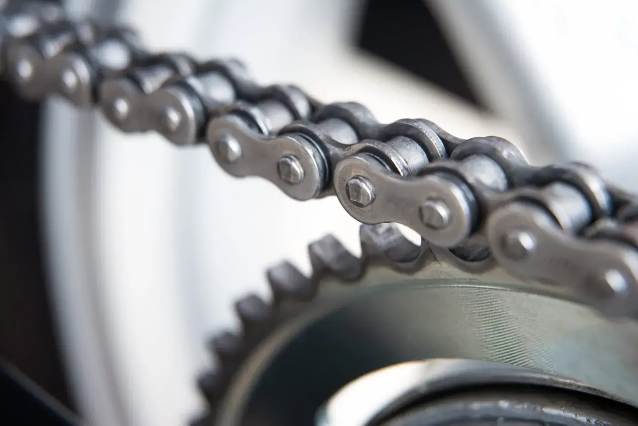 Metalowy łańcuch motocyklowy czeka na smarowanie. Widoczna zębatka sugeruje, że to kluczowy element napędu.