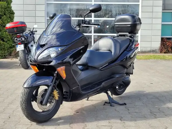 Czarny skuter Honda Forza 250 z kufrem na bagaż, zaparkowany przed budynkiem.