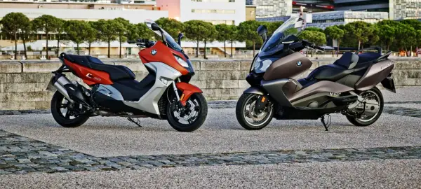 Dwa skutery BMW C650GT: jeden pomarańczowo-srebrny, drugi brązowy, stojące na kamiennym placu.