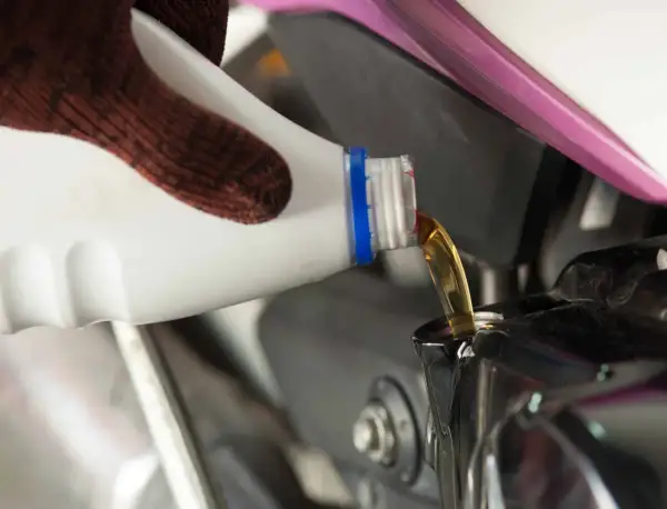 Rękawica wylewa olej do silnika motocykla. Pamiętaj, co ile wymieniać olej w motocyklu, by służył Ci długo.
