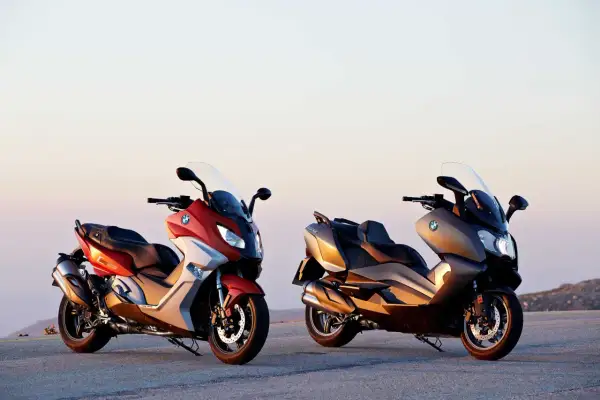 Dwa skutery BMW C650 Sport w kolorach czerwonym i brązowym stoją na tle zachodzącego słońca.