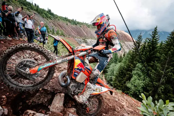Motocyklista walczy z kamienistym podjazdem podczas Erzberg Rodeo. Widzowie obserwują zmagania na stromym zboczu.