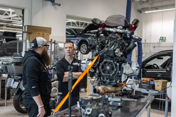 Mechanicy omawiają regulację linki sprzęgła przy silniku motocykla wiszącym na taśmach.