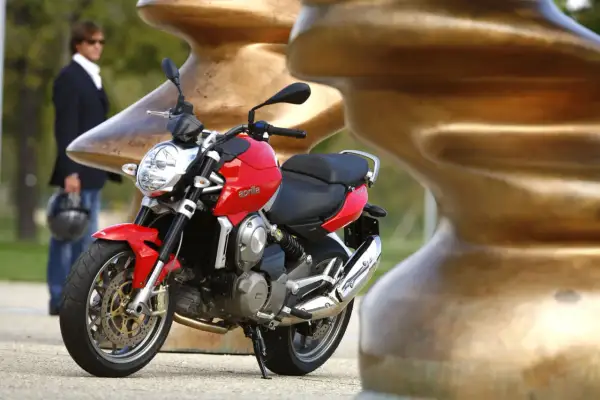 Czerwona Aprilia Mana 850 z chromowanym wydechem, obok mężczyzny w garniturze.