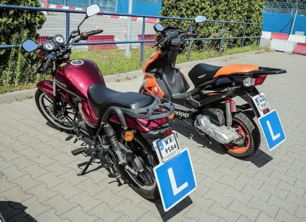 Dwa motocykle, jeden czerwony, drugi pomarańczowy, z literą "L" na tablicach. Idealne do nauki jazdy na kat. AM.