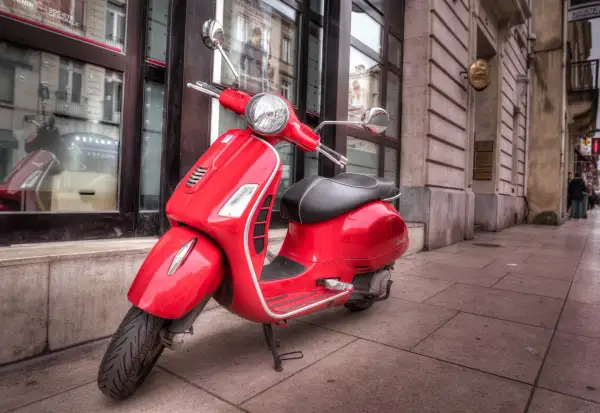 Czerwony skuter Vespa na chodniku. Karta motorowerowa od ilu lat? Warto sprawdzić, by legalnie poruszać się tym stylowym pojazdem.